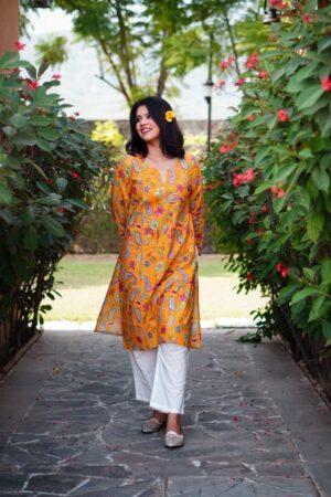 Woman walking forward wearing the Printed Pure Cotton Mustard Kurta Set in a floral walkway.